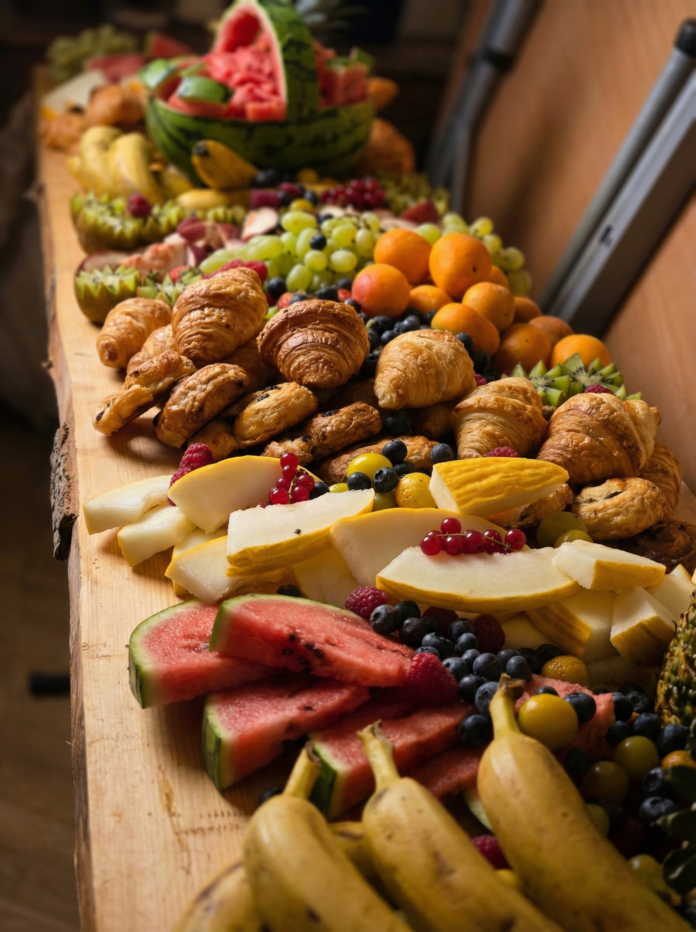 Buffet traiteur avec viennoiseries et assortiment de fruits frais présentés sur une planche.